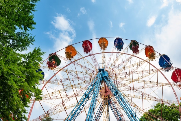 Ferris wheel in the green park over blue sky with clouds