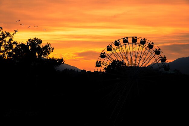 Photo a ferris wheel is silhouetted against a sunset sky with mountains in the background.