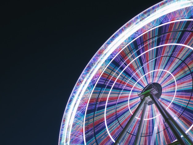 Ferris wheel at night long exposure light lines in a circle on a gradient sky background, copy space