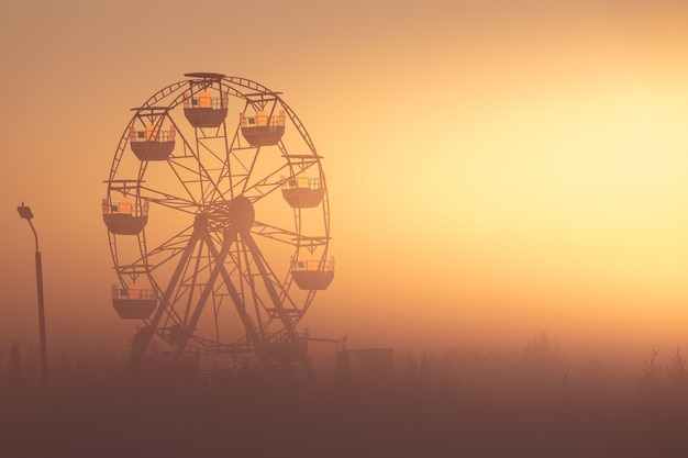 Ferris wheel in the park at dawn. Wonderful summer landscape. The sun's rays illuminate the morning mist.
