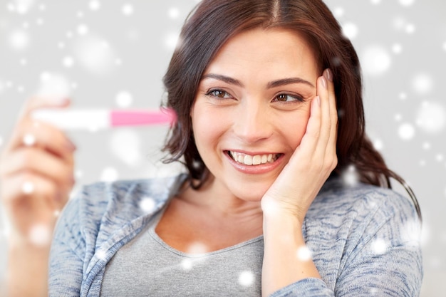 不妊、冬、出産、人々のコンセプト – 雪の上で自宅で妊娠検査を見ている幸せな笑顔の女性