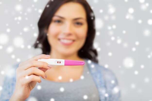 fertility, winter, maternity and people concept - happy smiling woman showing home pregnancy test over snow