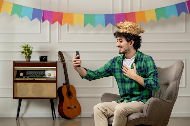 Festa junina cute young guy in straw hat with retro radio and colorful flags talking on videocall