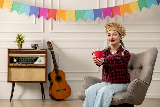 Festa junina schattig meisje in strohoed braziliaanse midzomer met retro radiogitaar die een rode kop geeft