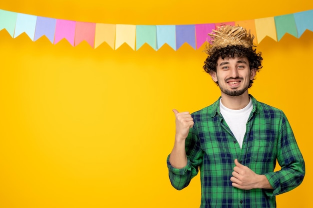Festa junina молодой симпатичный парень в соломенной шляпе и разноцветных флагах бразильского фестиваля счастлив