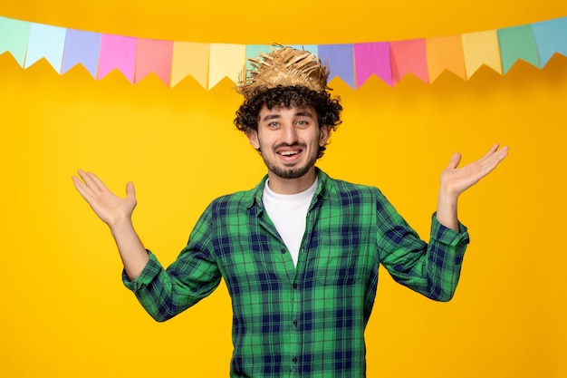 Festa junina молодой симпатичный парень в соломенной шляпе и разноцветных флагах бразильского фестиваля машет руками