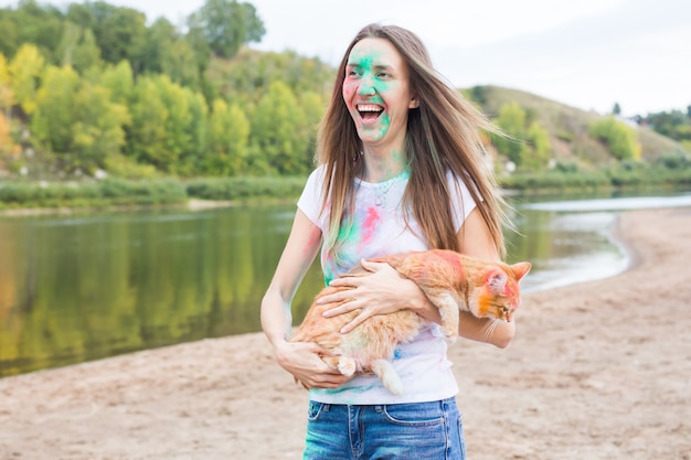 Festival holi, holidays, summer tourism and nature concept - young attractive girl with cat in coloured dust on natural background.