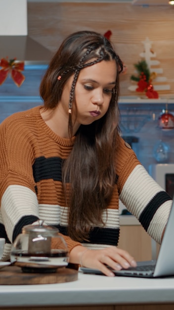 Festive adult typing on laptop while sitting in kitchen