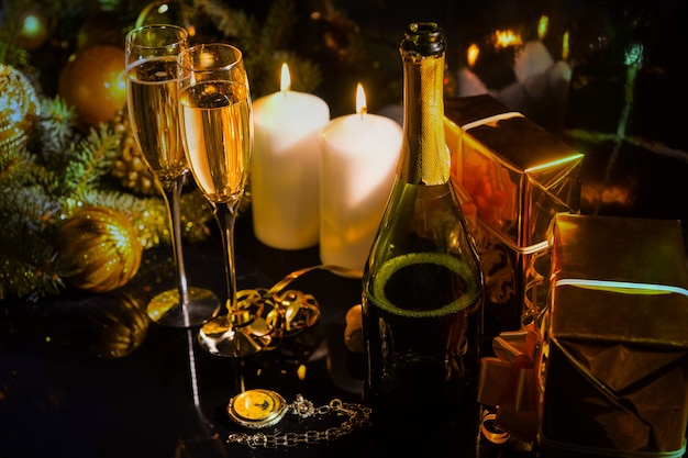 Festive arrangement for celebrating the New Year, with candles, champagne, pine branches, Christmas baubles and gift boxes wrapped in shiny golden paper