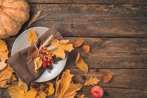 Foto fondo festivo di autunno con una zucca del tovagliolo delle posate del piatto e foglie di autunno su un fondo di legno