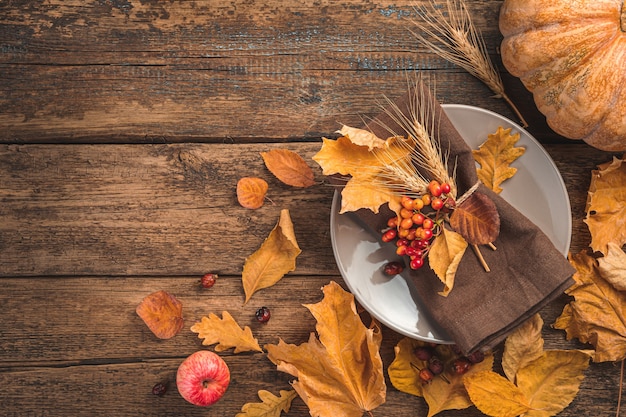 Фото Праздничный осенний кулинарный фон с тарелкой столовых приборов из тыквы и осенними листьями на деревянном фоне ...