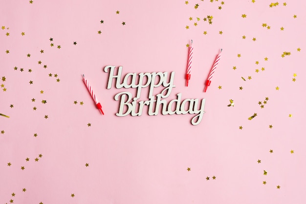 Festive backdrop from bright stars decoration, candles for cake and text Happy Birthday on a pink background.