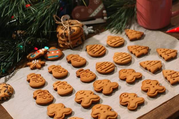 Sfondo festivo della panetteria di natale biscotti di pan di zenzero fatti in casa sulla teglia vicino alla decorazione del ramo di pino sul tavolo di legno primo piano celebrazione della famiglia e concetto di tradizioni di capodanno