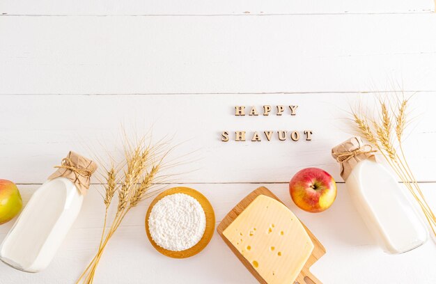 Festive background for the Jewish holiday of Shavuot dairy products apple ears of corn on a white background with a congratulatory text top view