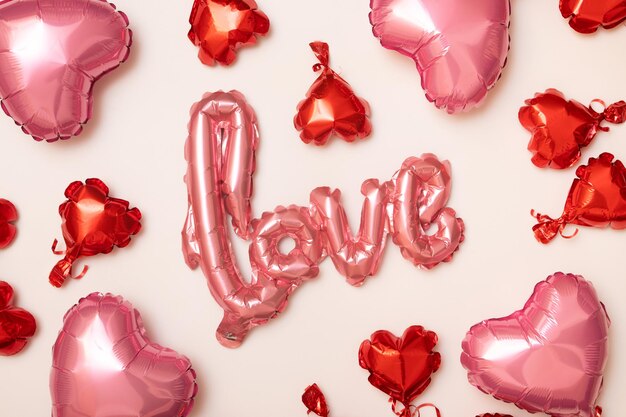 Festive background for Valentines Day from foil balloons shape heart and love word on beige background top view