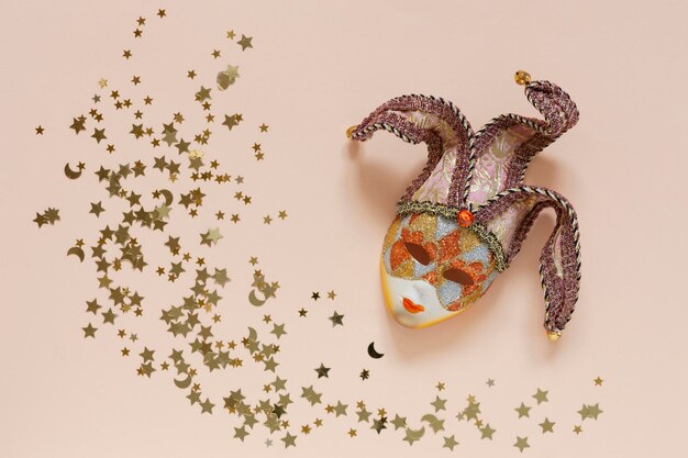 Фото Праздничный фон с карнавальной маской и конфетти с золотым блеском на фоне персикового цвета
