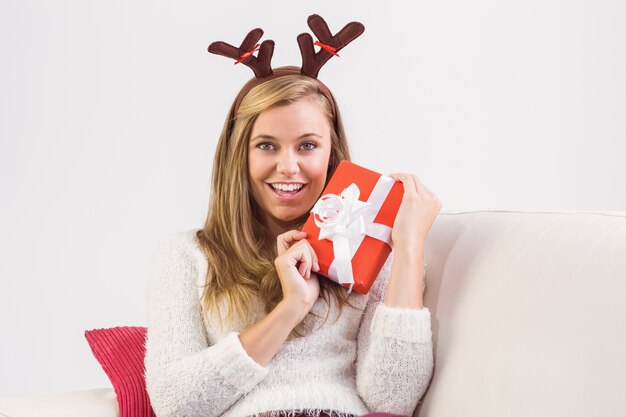 Festive blonde relaxing on sofa with gift