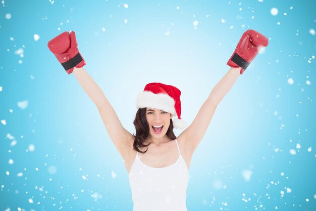 Festive brunette in boxing gloves cheering against blue vignette