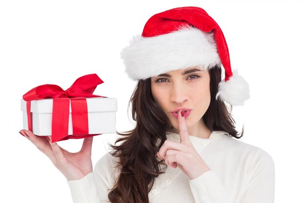 Festive brunette holding gift and keeping a secret