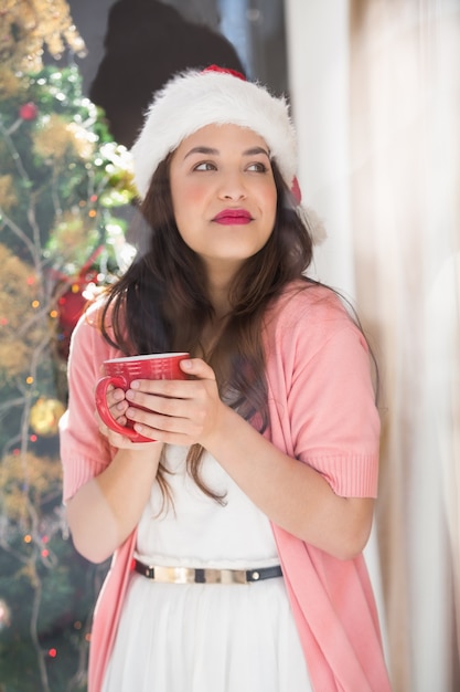 Festive brunette holding mug and thinking