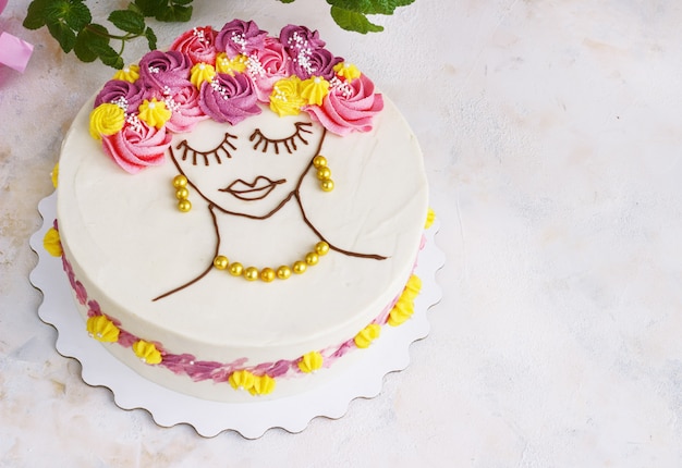 Torta festiva con crema di fiori e un volto di ragazza sulla luce