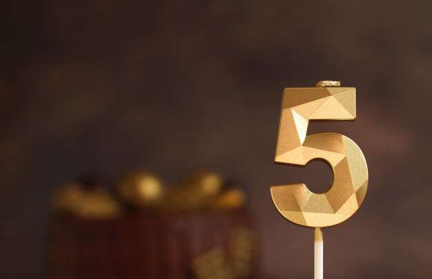 Festive candle number 5 on the background of a chocolate cake on a dark background