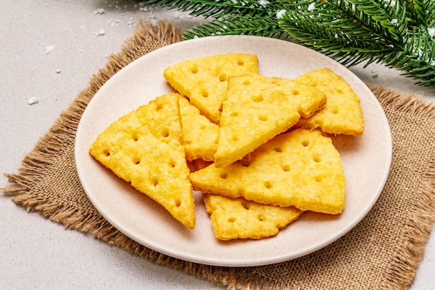 Festive cheese crackers, New Year snack concept. Cookies, fir tree branch, artificial snow, sackcloth napkin. Stone concrete background