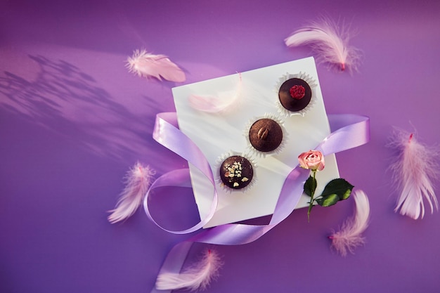 Caramelle al cioccolato festive delicate piume rosa con nastro viola sfondo con motivo di colore viola con ombre Foto Premium