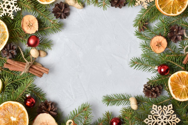 Festive Christmas background in the form of a frame. New Year's decor laid out in a circle. Christmas frame made of fir branches and cones, dried oranges, apples and wooden snowflakes.