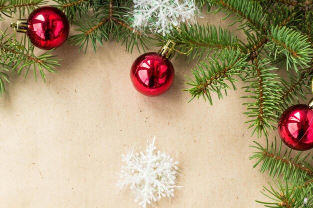 Festive christmas border with red balls on fir branches and snowflakes on rustic beige background