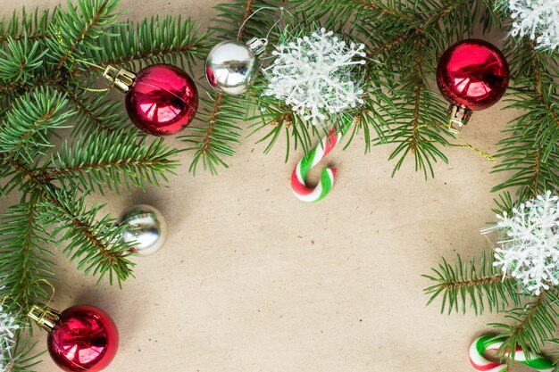 festive christmas border with red and silver balls on fir branches and snowflakes on rustic beige background with copyspace