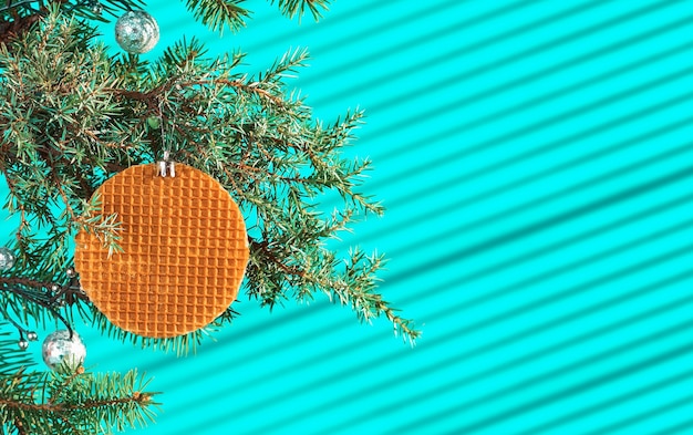 Photo festive christmas card, banner or postcard with branch of christmas tree with cones and decorated with waffle on turquoise table, streaks of light from the sun on the table, selective focus