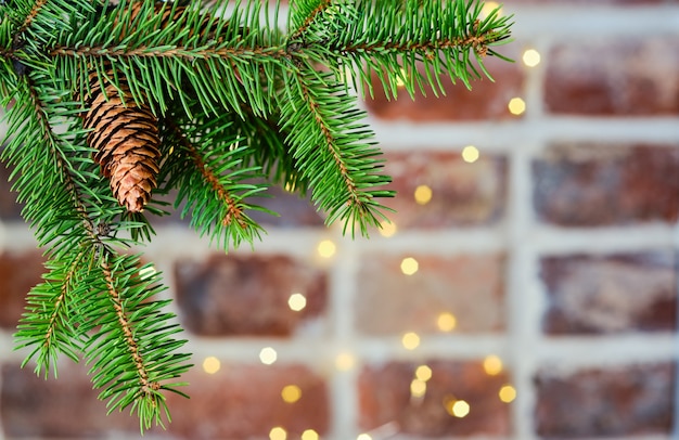 Festive Christmas card with a branch of a Christmas tree on a table of a brick wall decorated with a garland, selective focus.