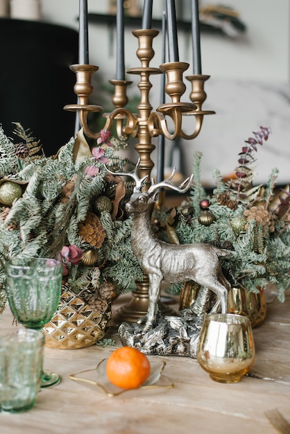 Foto festosa cena di natale con candele souvenir di cervo in un candeliere, bicchieri di mandarino e rami di abete o abete rosso in un vaso