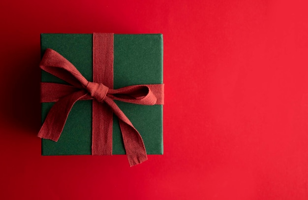 Праздничная рождественская подарочная коробка, перевязанная деревенской лентой и бантом на красном фоне. Вид сверху.