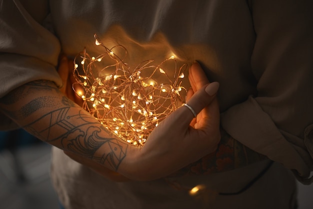 Festive Christmas lights garland in female hands on a dark background