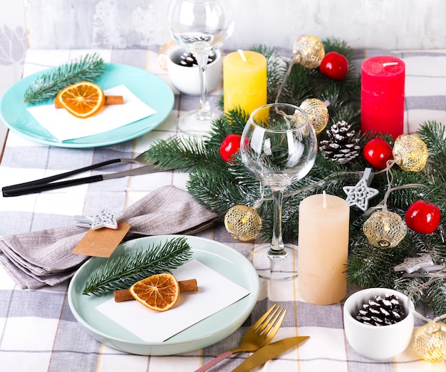 Festive Christmas and New Year table setting with dry orange and cinnamon on a gray textile. Dining place decorated with pine cones, branches and candles