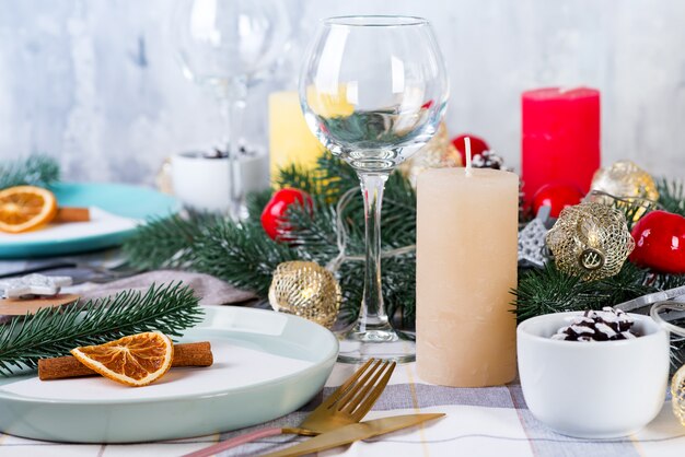 Festive Christmas and New Year table setting with dry orange and cinnamon on a gray textile. Dining place decorated with pine cones, branches and candles