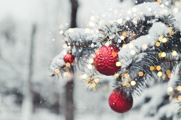 Festive Christmas tree decorated with glass red toy balls with golden highlights. Winter landscape with snow and christmas trees.