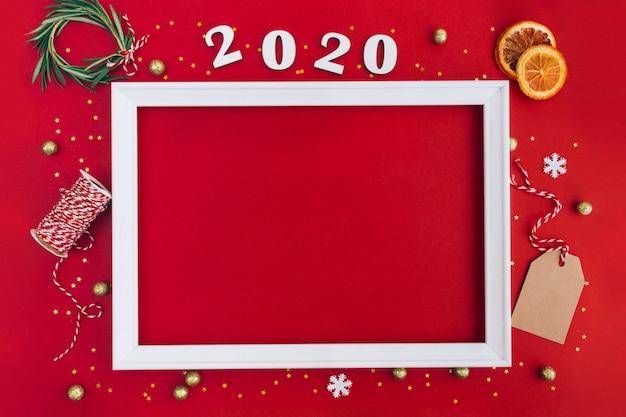 Festive christmas white frame made of christmas decorations and 2020 wooden numerals on red background with copy space.