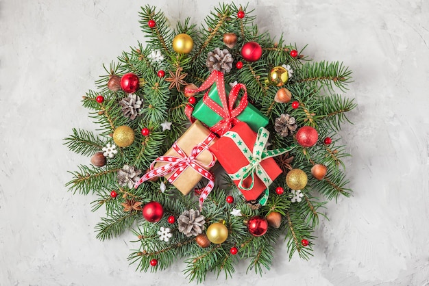 モミの木とコンクリートの背景にギフトボックス付きの休日の装飾で作られたお祝いのクリスマスリース。クリスマス、新年あけましておめでとうございますのコンセプト。上面図。フラットレイ