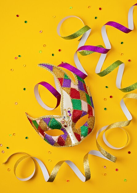 Festive, colorful mardi gras or carnival mask and accessories over yellow wall. Flat lay, top view, copy space