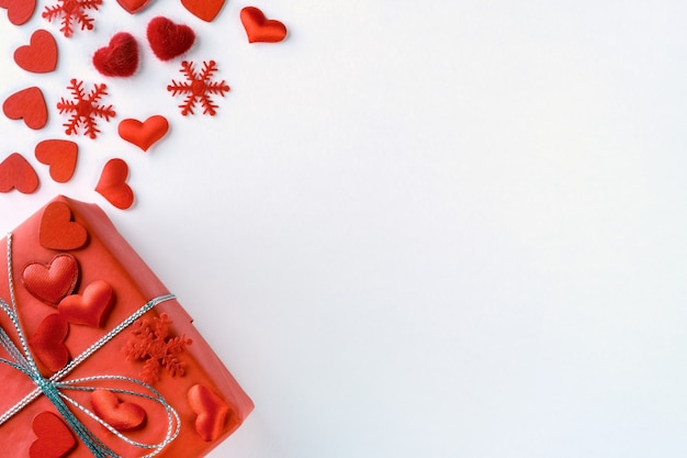 Composizione festiva da regalo rosso legato, fiocchi di neve e cuori sparsi su bianco per san valentino