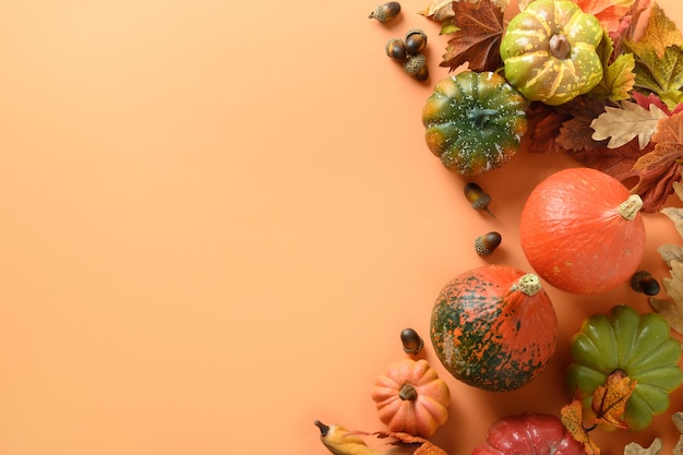 Festive composition of pumpkins, colorful leaves on orange background with space for text. Thanksgiving Day and Halloween template. View from above.