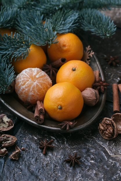 Foto contenuto festivo, mandarini, noce, cannella, cardamomo, piatto di metallo, ramo di abete, sfondo marrone scuro, verticale