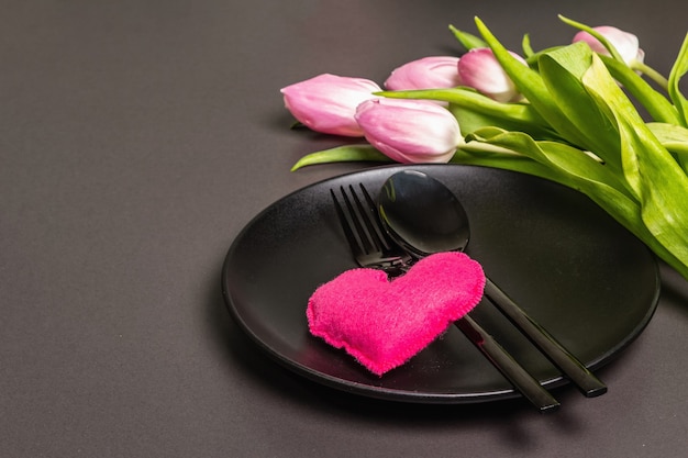 Festive creative black table setting with tulips and felt heart on dark background