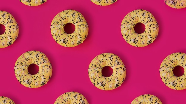 Праздничный творческий узор из рядов желтых пончиков на розовом фоне