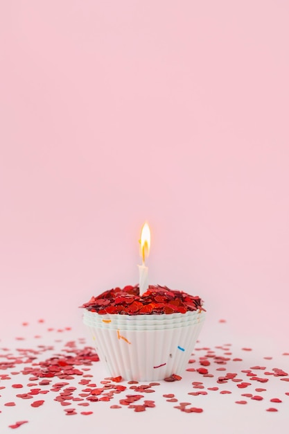 ピンクの背景に燃えるろうそくとお祝いのカップケーキ休日のバレンタインデーのグリーティングカード