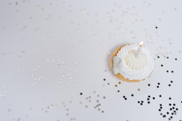 Festive cupcake with one burning candle on a white plain background with confetti stars Celebration birthday party congratulations card