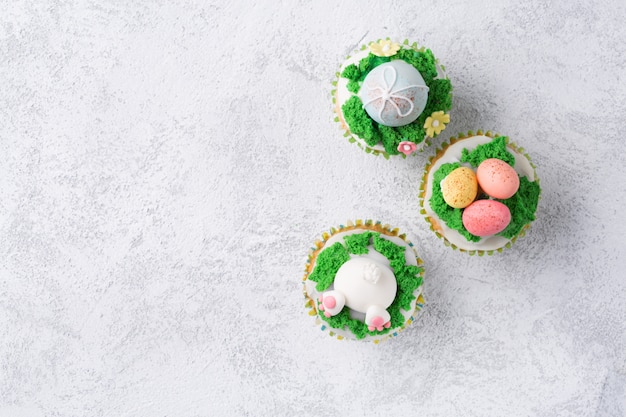 Festive cupcakes with funny bunny, eggs and grass on white background. Easter holiday concept. Top view with copy space